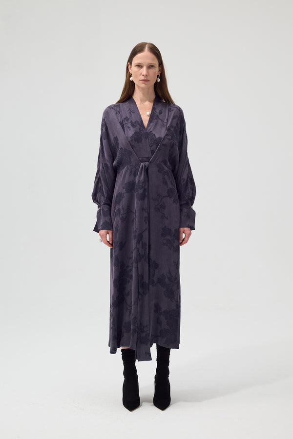 Woman wearing a long, dark purple dress with a subtle pattern on a white background