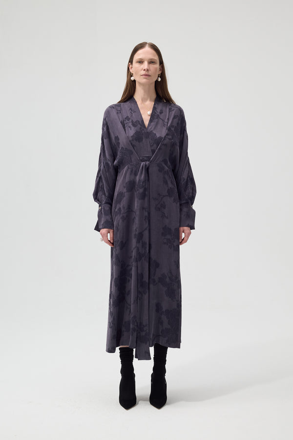 Woman wearing a long, dark patterned dress on a white background